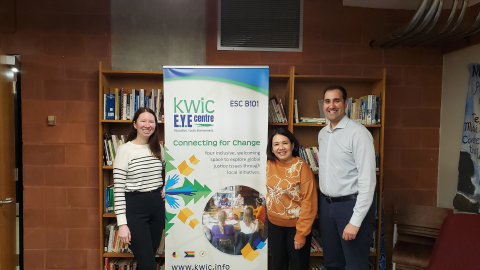 Sam (left) stands with Carmela (middle) and Ryan (right) in front of a KWIC banner